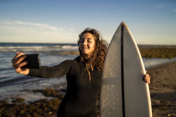 istock Selective focus shot of a smiling female taking selfies from her phone while holding a surfboard 1439180101