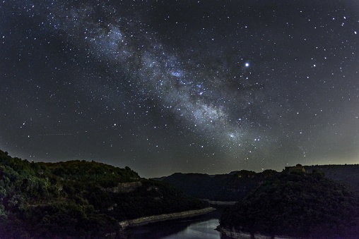 The water stream surrounded by hills under the starry night sky