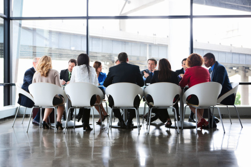 Businessmen and women of varying ethnicities and ages meeting at large conference table in modern glass office. Copy space. CLICK FOR SIMILAR IMAGES AND LIGHTBOX WITH BUSINESS PEOPLE. 