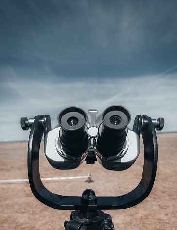 A closeup vertical shot of a public binoculars on a blue sky and dry grassland backgrounds