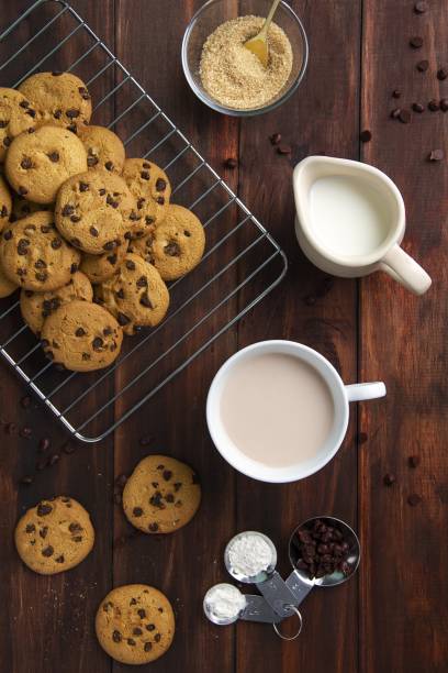 High angle shot of Chocolate chip cookies, milk in a jug and coffee in a cup on a wooden table
