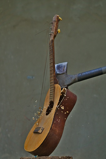 A vertical image of an axe smashing an acoustic guitar