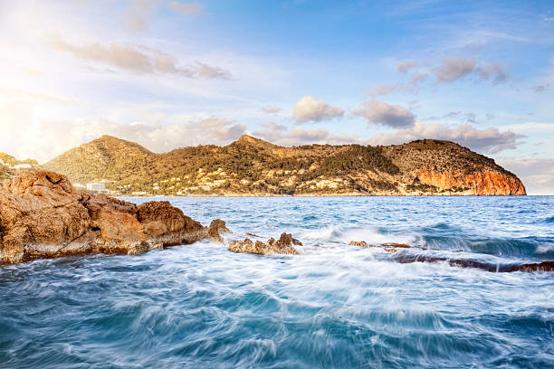 The sea seen to the horizon from a rocky beach with waves crashing on the shore