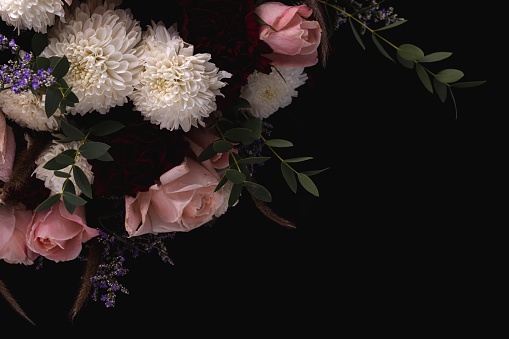 A closeup shot of a luxurious bouquet of pink roses and white, red dahlias on a black background