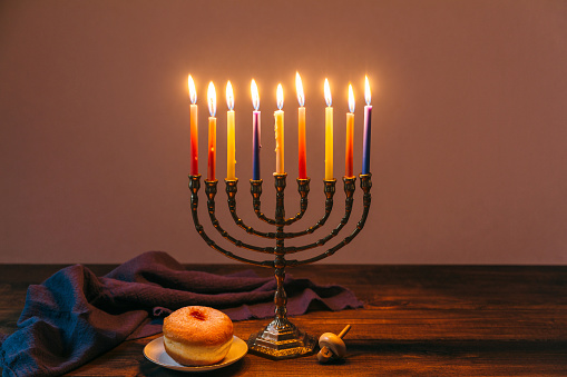 Jewish Holiday Hanukkah background with traditional candelabra menorah, candles, donuts and dreidels on wooden table background