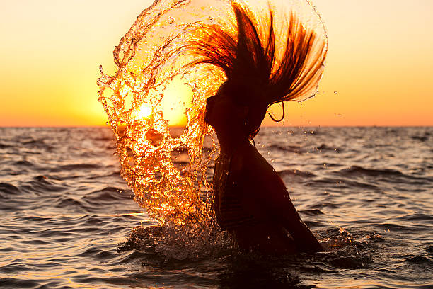 teenage girl standing in the sea in a bathing suit, tossing her wet hair in the spray, alone, bathing, her back turned