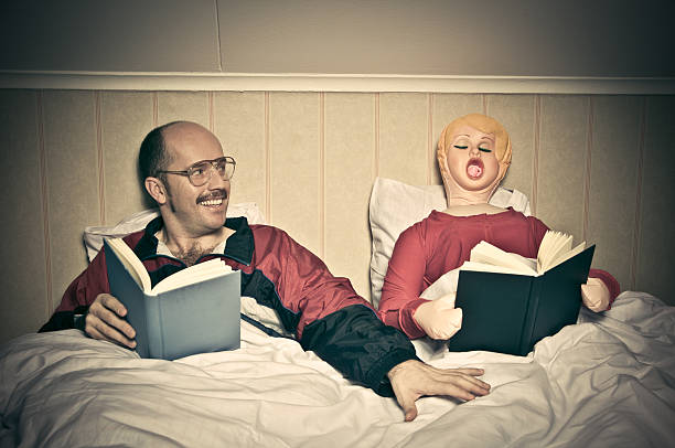 Bed Time Routines Nerdy looking guy and blow up doll reading in bed blow up doll stock pictures, royalty-free photos & images