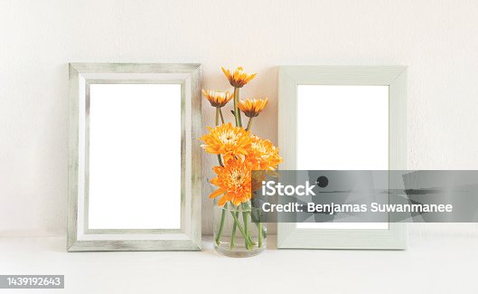 istock Two light green rectangle border photo frame and orange flowers (chrysanthemum) in vase on a wooden shelf. 1439192643