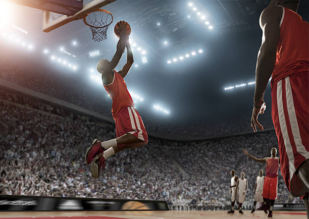 Basketball Player Scores During Game professional  basketball player jumping with ball about to score in indoor floodlit arena basketball player photos stock pictures, royalty-free photos & images