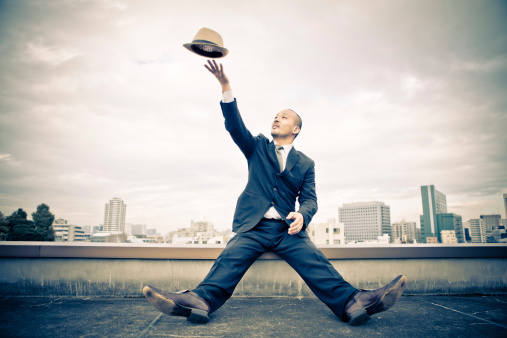 Japanese businessman tossing his hat in the air on a rooftop in Tokyo with the financial district in the background.