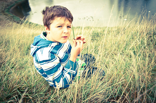 Boy in nature whistles with a blade of grass