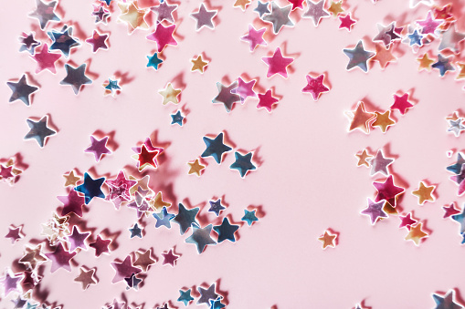 Multicolor holographic Stars Glitter Confetti on pink background. Festive backdrop, selective focus.