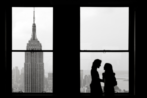 View of The Empire State Building from the Rockafeller Center. Two people in silhouette in front of the window