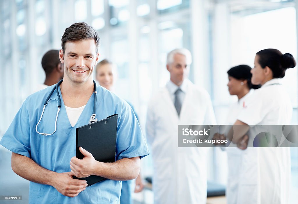 Bell'infermiere uomo con il personale medico in sottofondo - Foto stock royalty-free di Infermiere uomo