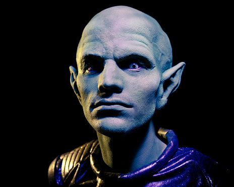 A head and shoulders portrait of an alien man with a bald head and pointed ears. Horizontal shot.