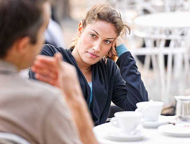 Couple Talking at a Cafe A woman listening to a man (defocussed) talking during a discussion at an outdoor cafe. bad coffee stock pictures, royalty-free photos & images