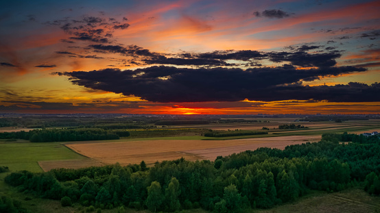 Colorful sunset over forest and fields aerial with sun and distant power wind stations, Podlaskie Voivodeship, Poland, Europe