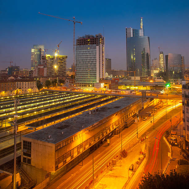 Downtown Milan, Italy. View over the major Porta Garibaldi Station with motion blured cars on the streets around the train and subway station. Illuminated business and office skyscrapers, together with new skyscraper construction site in the background. Milan at twilight, blue hour.