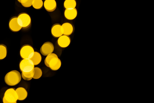 Golden blurred lighs bokeh on black background as a festive backdrop, night defocused light spots