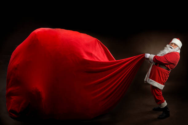 Santa Claus holding a BIG gift bag. On dark background 