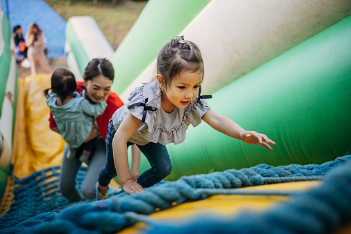 Three people, Japanese woman with her two little daughters having fun in inflatable bouncy castle in amusement park.