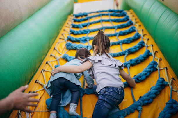 Cute little sisters playing in inflatable bouncy castle in amusement park.
