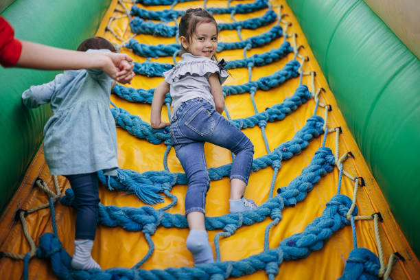Cute little sisters playing in inflatable bouncy castle in amusement park.