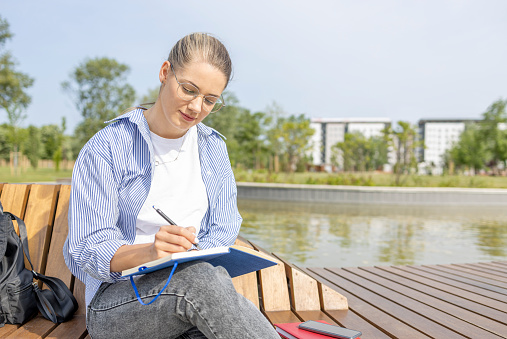 Young woman studying in the park, taking notes when studying