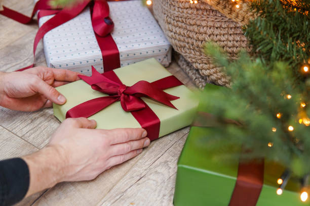 Man putting Christmas gift box under Christmas tree in living room.
