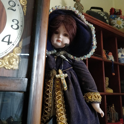 Old doll in purple next to antique clock
