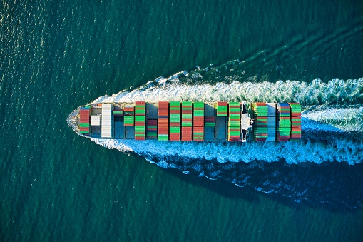 An aerial shot of an industrial ship sailing in the turquoise ocean