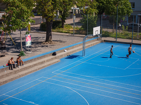 BASEL, SWITZERLAND, JULY 7, 2022: men play basketball in the city center, on the new blue court in the park