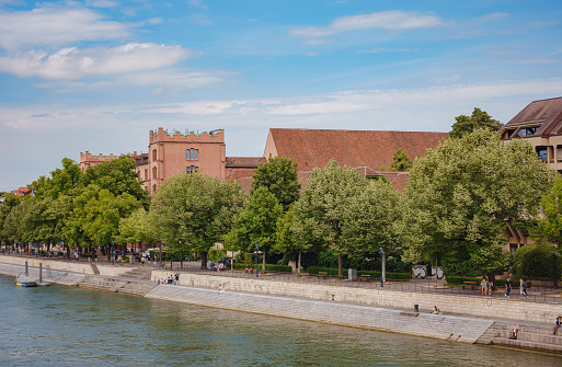 BASEL, SWITZERLAND, JULY 7, 2022: Buildings in the city centre of Basel and the Rhine river, Switzerland. Riverside of swiss city. people walk and relax over river