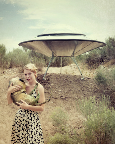 Tabloid style image of retro 50's woman holding a newly found baby alien at UFO landing site.