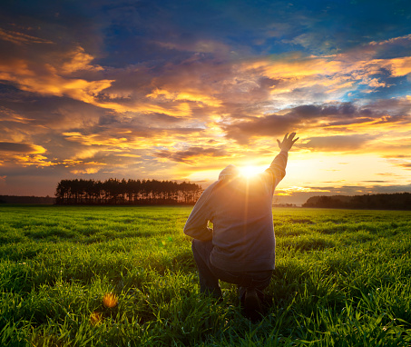 Man prays to God - man on a green field and sunset