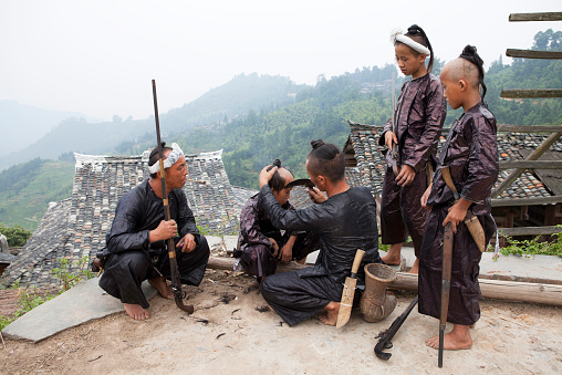 Miao tribe man cut the kids hair with a big knife,Biasha (Basha) Miao Village,Congjiang,Guizhou Prrovince,China.
