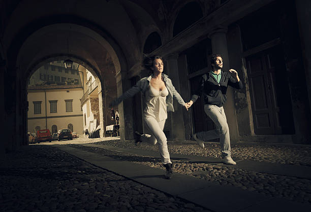 couple running scare couple running thru an ominous street tunnel in small town of northern italy as someone bad was chasing them. escaping stock pictures, royalty-free photos & images