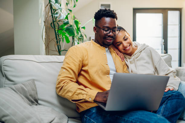 istock Multiracial couple using laptop while sitting on a sofa at home 1439215104