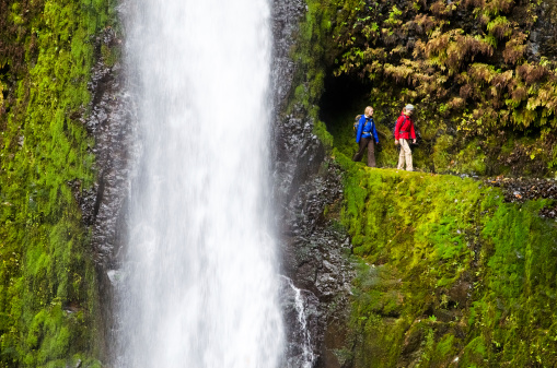 Two hikers emerge from a tunnel behind a waterfall. Tunnel Falls, Eagle Creek Trail, Oregon.