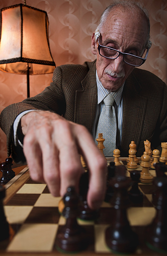 One old man playing chess in his humble living room. More files of this model and series on port. Made with professional equipment. Vertical format in shallow depth of field.