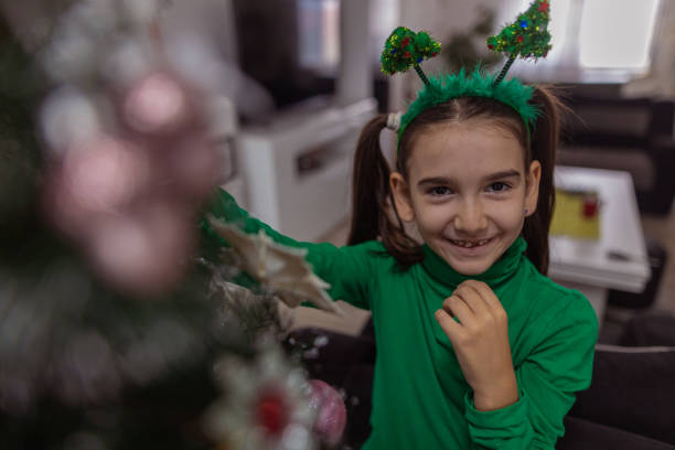 Little girl with tiara decorating Christmas tree at home.