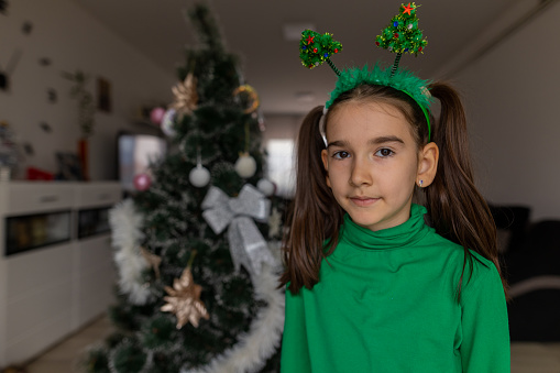 Little girl with tiara decorating Christmas tree at home.