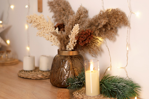 Eco-friendly New Year and Christmas home decor.A bouquet of dried flowers in a glass vase, lighted candles, fir branches on the table.Selective focus,close up.