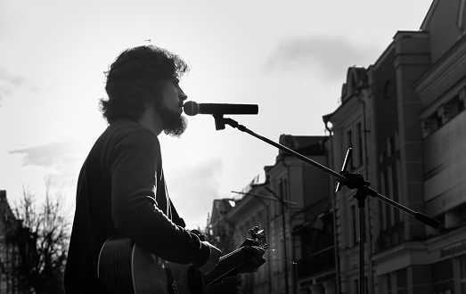 Street musician singing in microphone on blurred background of city street buildings and gray sky. Black and white image. Ukraine, Zhytomyr, November, 04, 2022