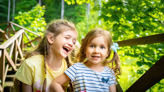 Beautiful children close up. Positive happy emotions in kids. Two girls laugh against the background of green trees. The concept of a carefree happy childhood. Children with happy facial expressions.
