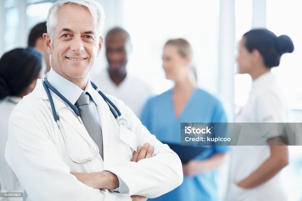 Médico bem sucedido sênior sorrindo com as mãos dobradas - Foto de stock de Adulto royalty-free