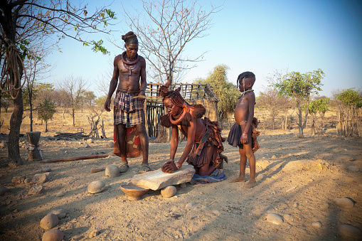 The mother is grinding maize with a stone to make flour. There is some motion blur of the woman's head and hands as she works.