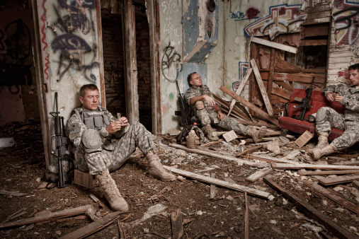 A group of U.S. Army soldiers sit on the floor of an abandoned building while taking refuge from the battle.