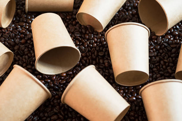 maquette de tasses à café jetables couchées sur des grains de café. quelques tasses à café en papier vides - consumerism ground coffee packaging coffee photos et images de collection