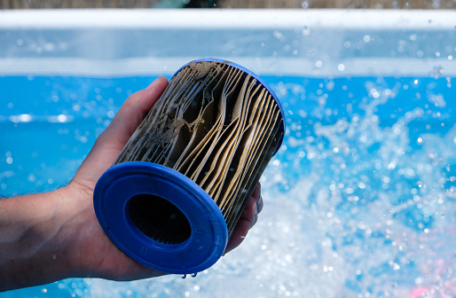 Dirty Replacement Pool Filter Cartridge in a man's hand on water splash background. Pool water quality concept. Copy space.